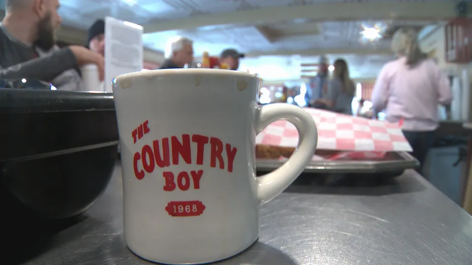 A Country Boy 1968 logo mug on the counter of the busy diner, tin ceiling overhead.