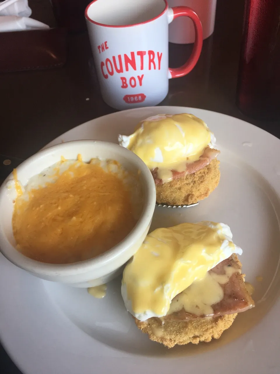 The Backyard Bennie: poached egg and hollandaise over fried green tomato and country ham, grits on the side, a Country Boy mug behind.