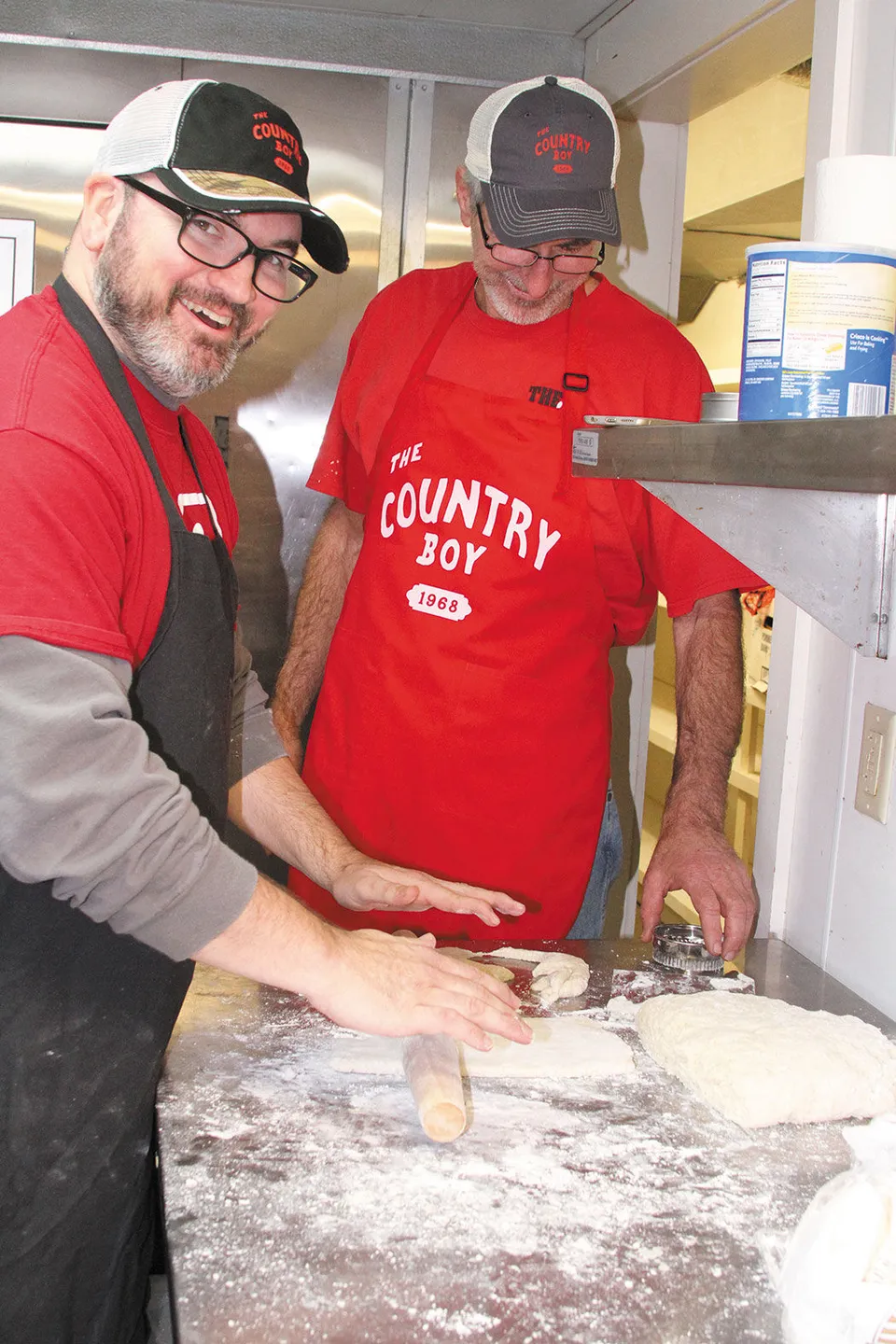 The 2016 owners in red Country Boy tees and aprons, rolling biscuit dough in the kitchen.
