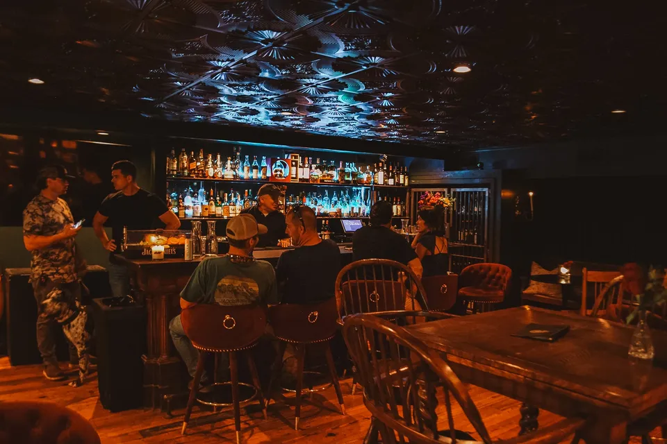 The bar on a show night: the backbar lit blue under the pressed-tin ceiling, every stool taken.