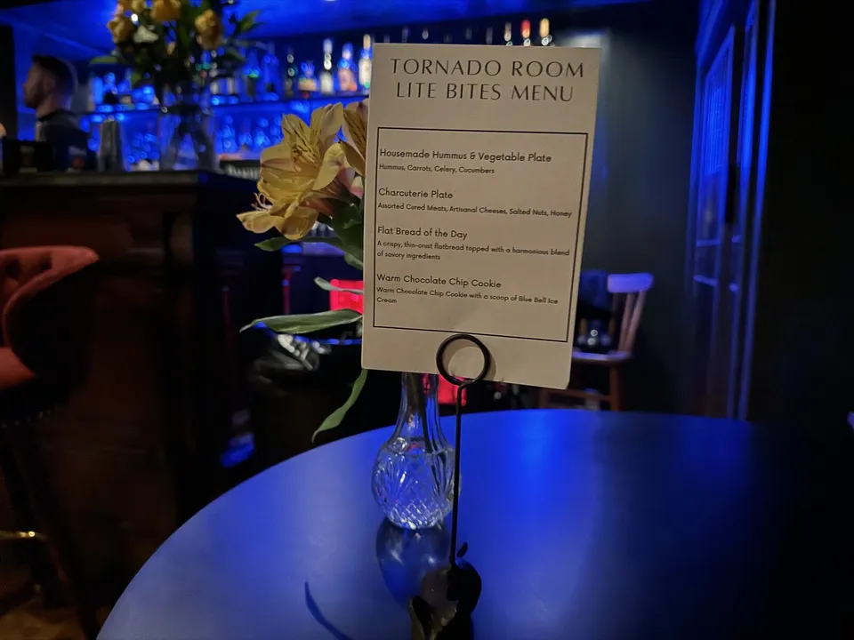 The printed Tornado Room lite bites card on a table, the blue-lit backbar behind it.