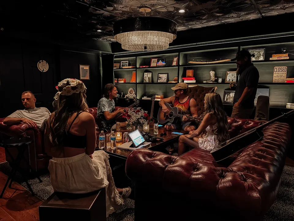 The lounge, full: guests on the oxblood Chesterfields, a guitar being passed around under the chandelier.