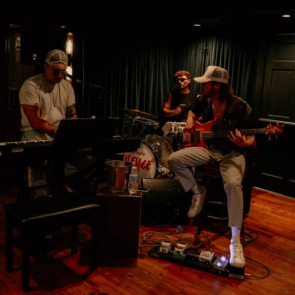 A trio on stage: keys out front, guitar and bass behind, the room dark around them.
