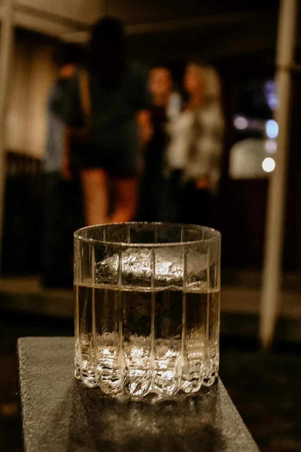 A rocks glass of whiskey on the bar, the lounge soft behind it.
