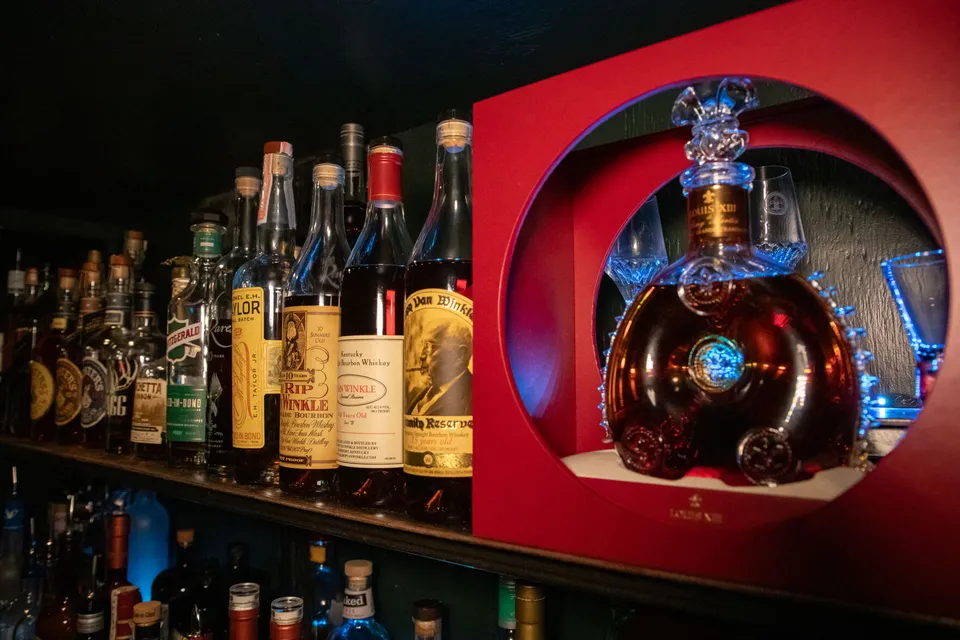 The whiskey shelf: a lineup of aged bourbons and a cognac in a lit red display case.